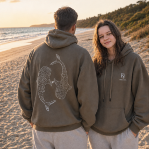 Couple wearing matching KJ The Label whale shark hoodies on the beach at sunset